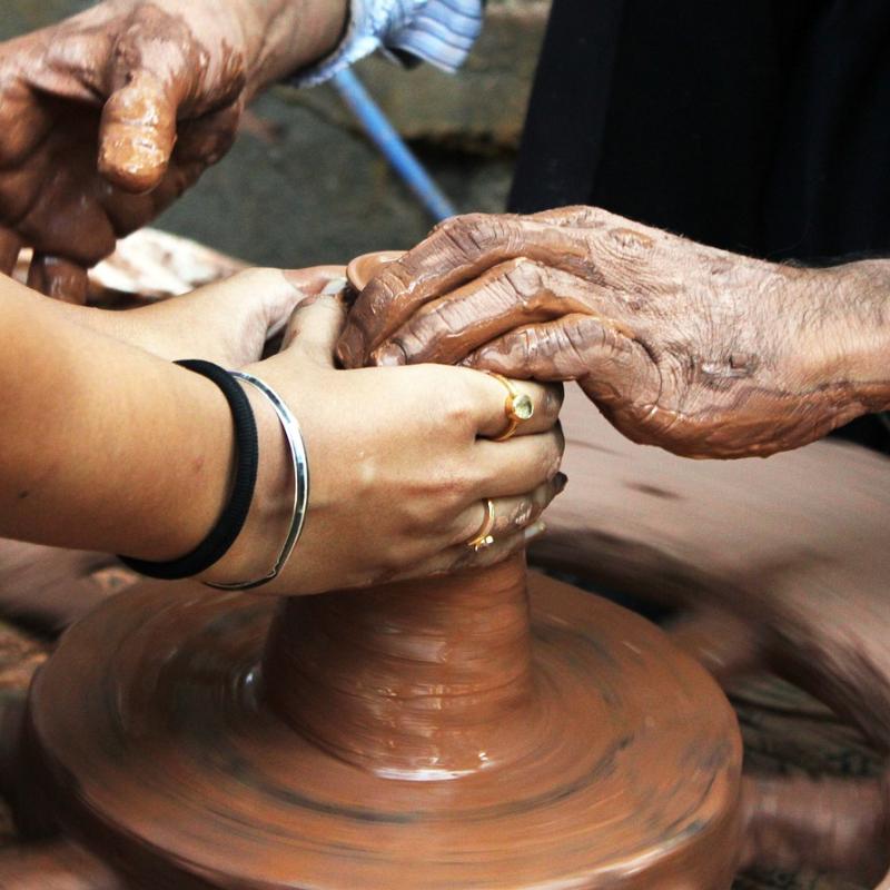 Older hands helping younger hands on a pottery wheel